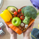 Heart dish with healthy foods, weights, scale, and sports shoes in fitness center.