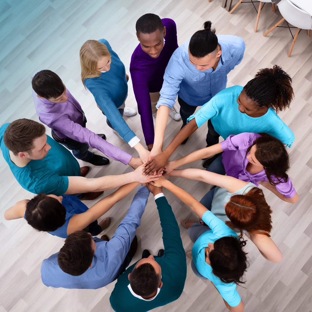 Diverse team members standing in a circle, joining hands in a collaborative gesture on a wooden floor.