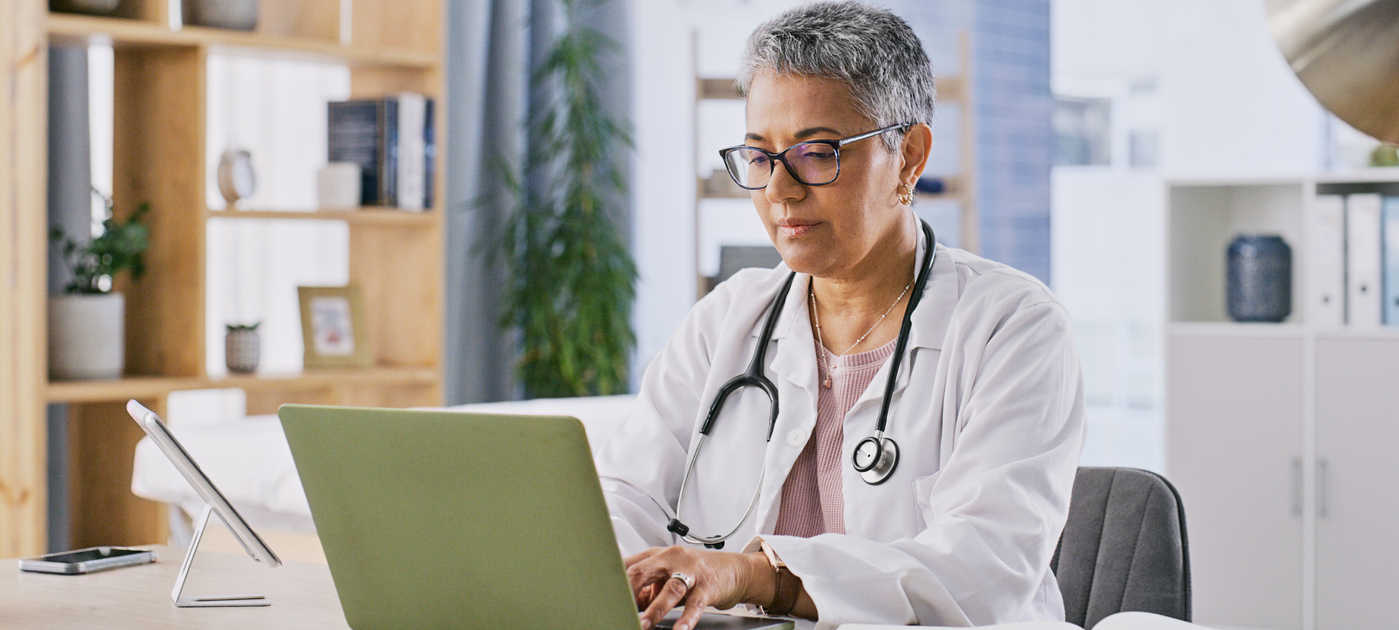 Laptop, doctor and mature woman typing research on healthcare, clinic medicine or medical study. Hospital, computer and surgeon search online for cardiology report, health info or nursing service